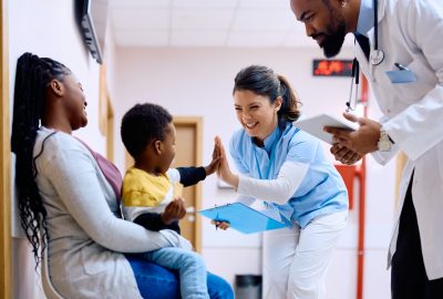 Happy nurse giving high-five to small black boy at medical clinic.